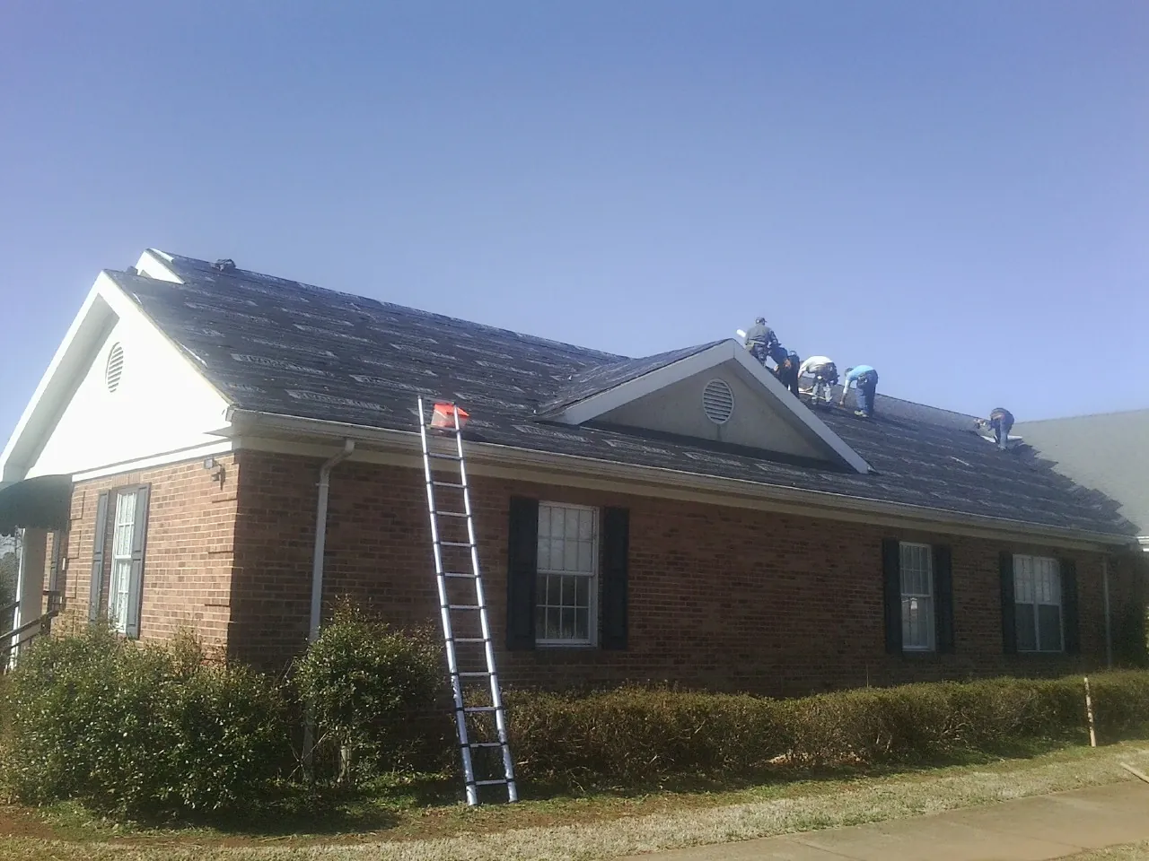 Crew tearing shingles off a brick ranch roof with a ladder set — Metal Roof Repair work by our crew in Cordova