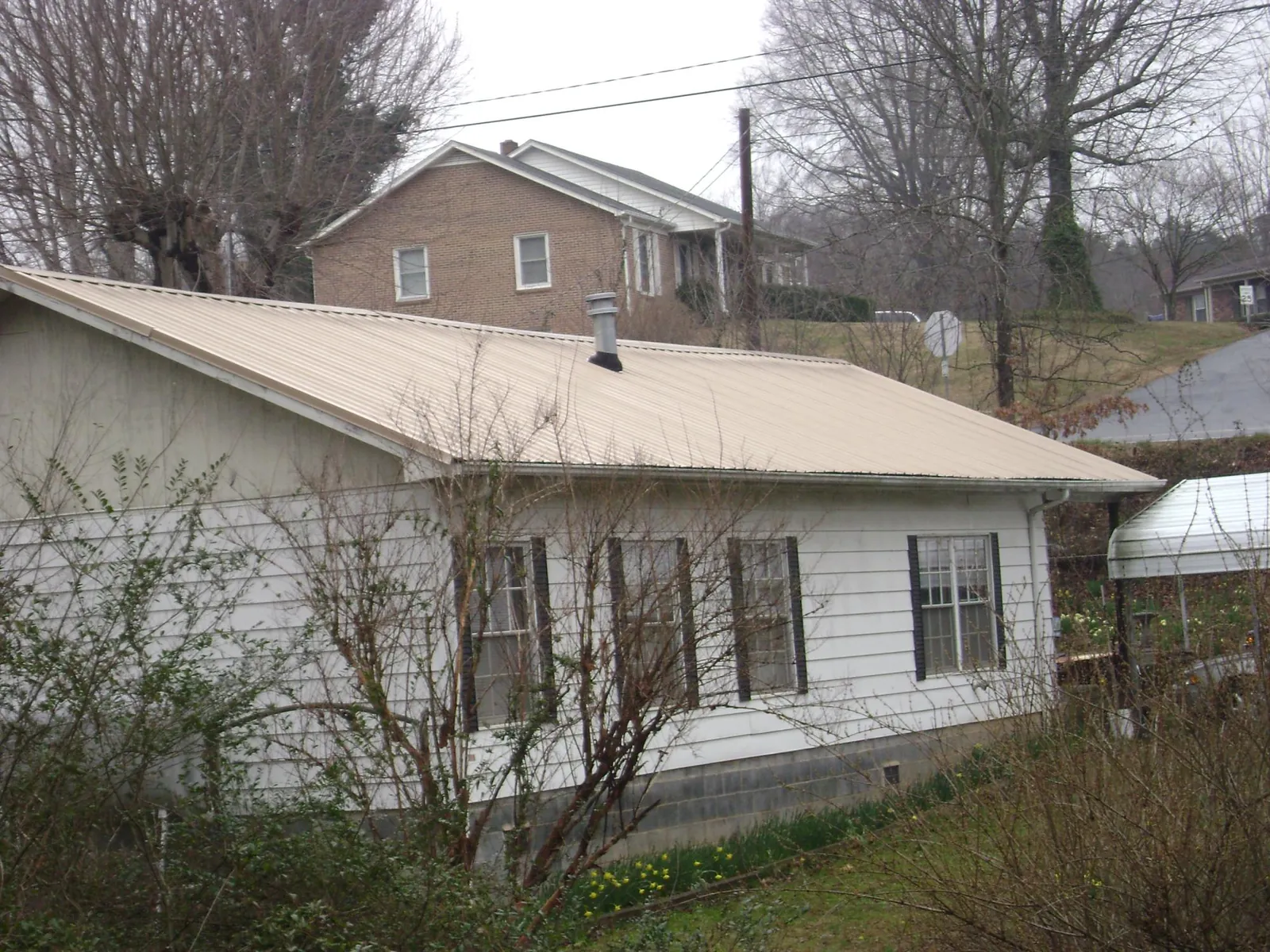Tan metal roof on a white sided house set into a hillside — Commercial Roofing by Roofing Brothers in Cordova